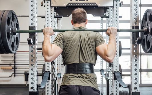 Athlete rests a loaded bar across their upper back, preparing to squat.