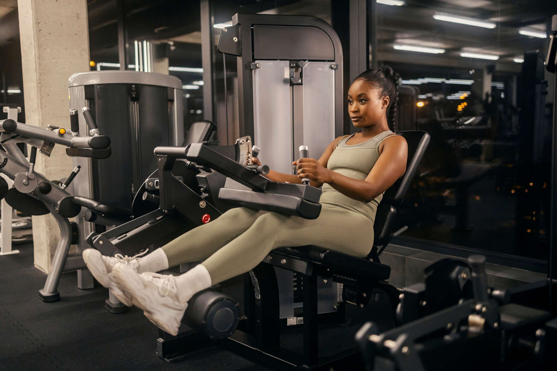 Athlete works on a seated leg curl machine in a gym.