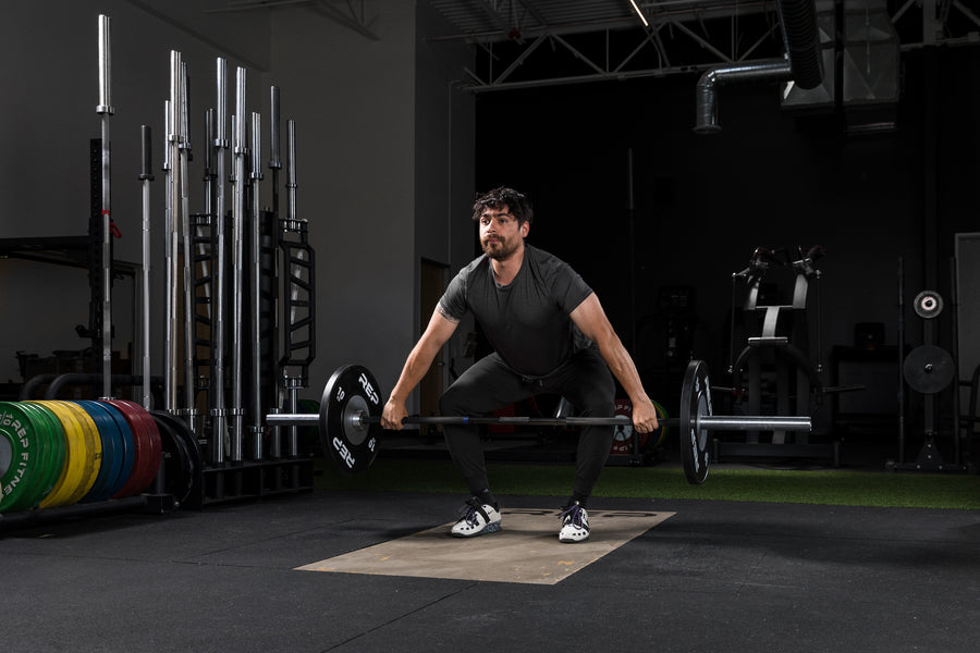 Athlete hang lifting a barbell with Black Competition Bumper Plates (KG)