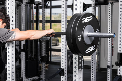 Athlete holding a barbell with Black Competition Bumper Plates (KG) on the front of a PR-5000 rack