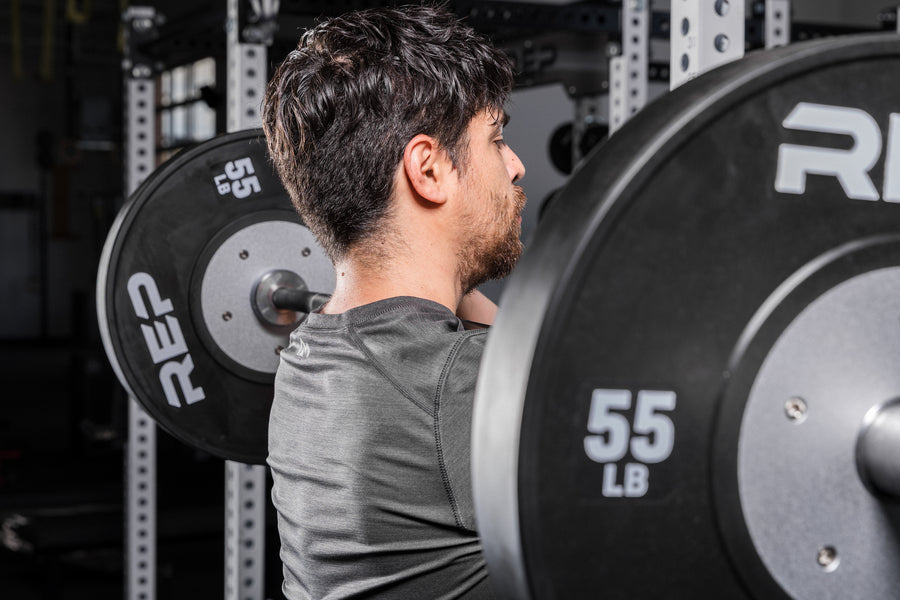 Athlete holding a barbell with Black Competition Bumper Plates (LB) in a front rack position