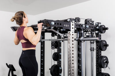 Person performing pull-ups off the front of the Summit™ All-In-One Ares™ 2.0 configuration utilizing the brackets +. pull-up bar in a gym setting.