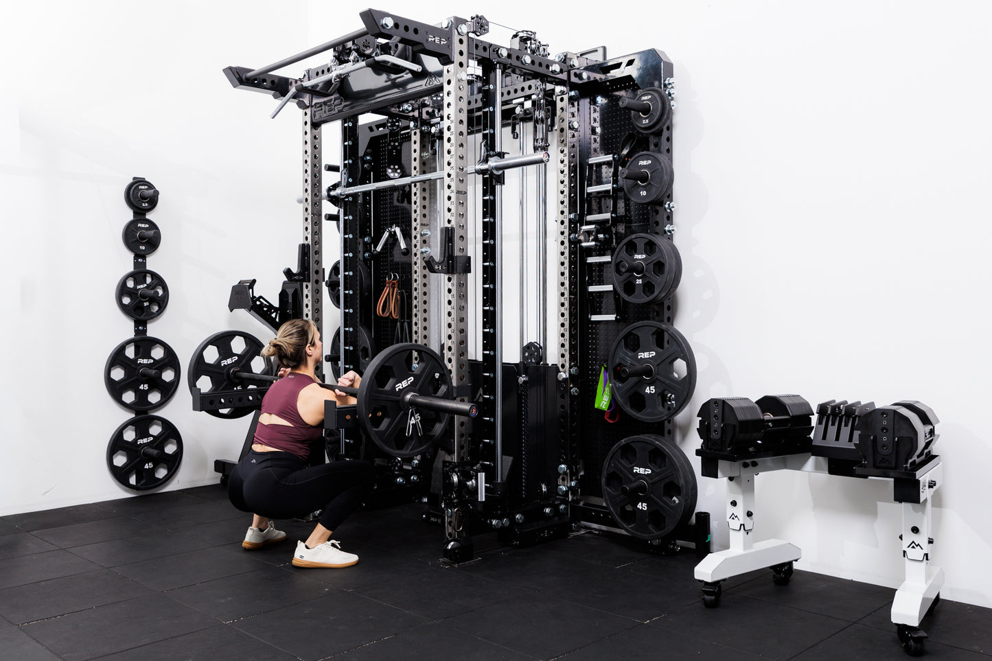 Person performing front squats off the front of the Summit™ All-In-One Ares™ 2.0 Wall-Mounted configuration in a gym setting.