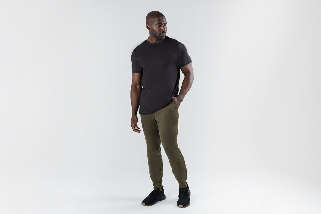 The REP Fitness Men's Attis Joggers in Heather Olive front, black tee, hand in pocket