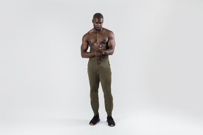 The REP Fitness Men's Attis Joggers in Heather Olive front, shirtless, adjusting drawstring