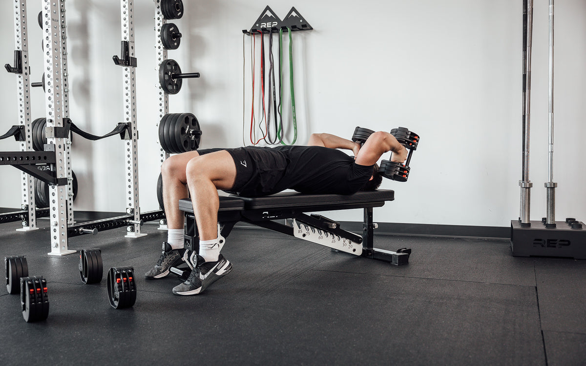 Male lifter lying on a bench and performing skull crushers with a pair of REP Fitness QuickDraw Adjustable Dumbbells.