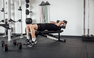 Male lifter lying on a bench and performing skull crushers with a pair of REP Fitness QuickDraw Adjustable Dumbbells.