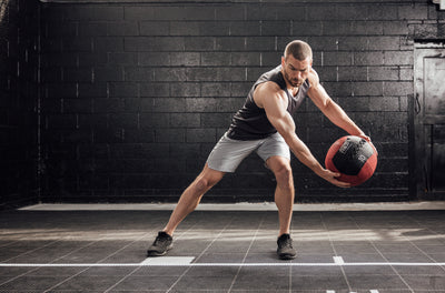 The REP Fitness Men's Sigmatech Tank Top in Heather Black front, throwing med ball