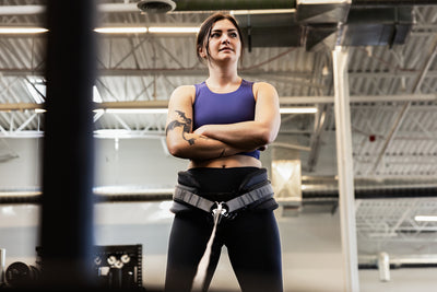 Woman in a gym wearing a sports bra and leggings with a weightlifting belt squat belt on.