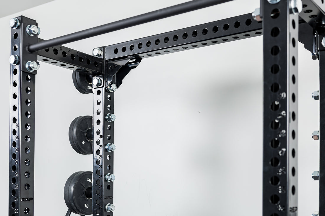 Close-Up of Compact Logo Plate Crossmember 2.0 on a REP power rack with weights on a white background.