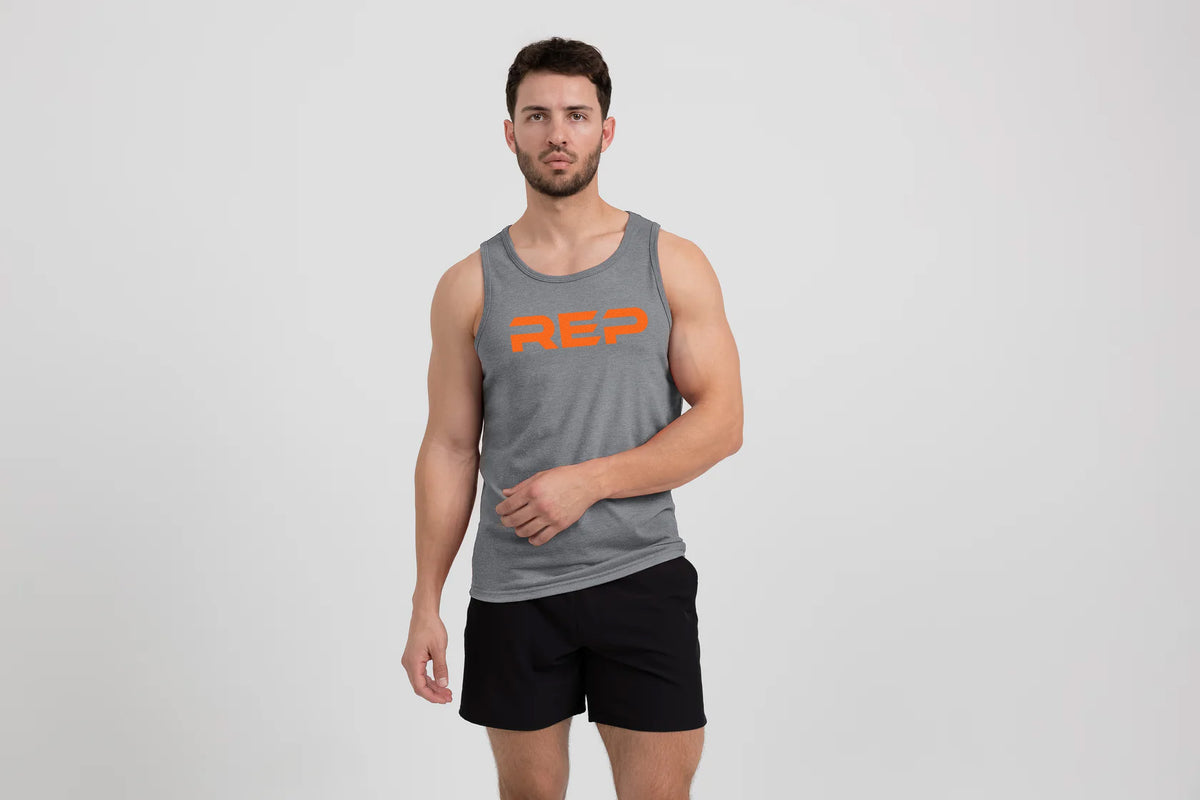 Man wearing the Men's Daily Driver Tri-Blend Tank in Heather Aluminum/Orange with shorts