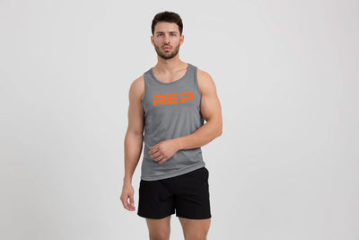 Man wearing the Men's Daily Driver Tri-Blend Tank in Heather Aluminum/Orange with shorts