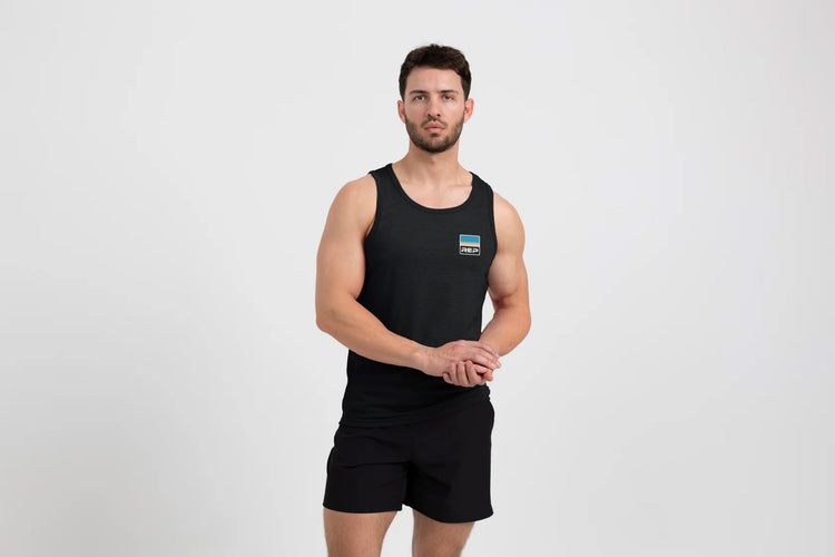Man wearing a black Men's Rise Tri-Blend Tank and shorts on a white background