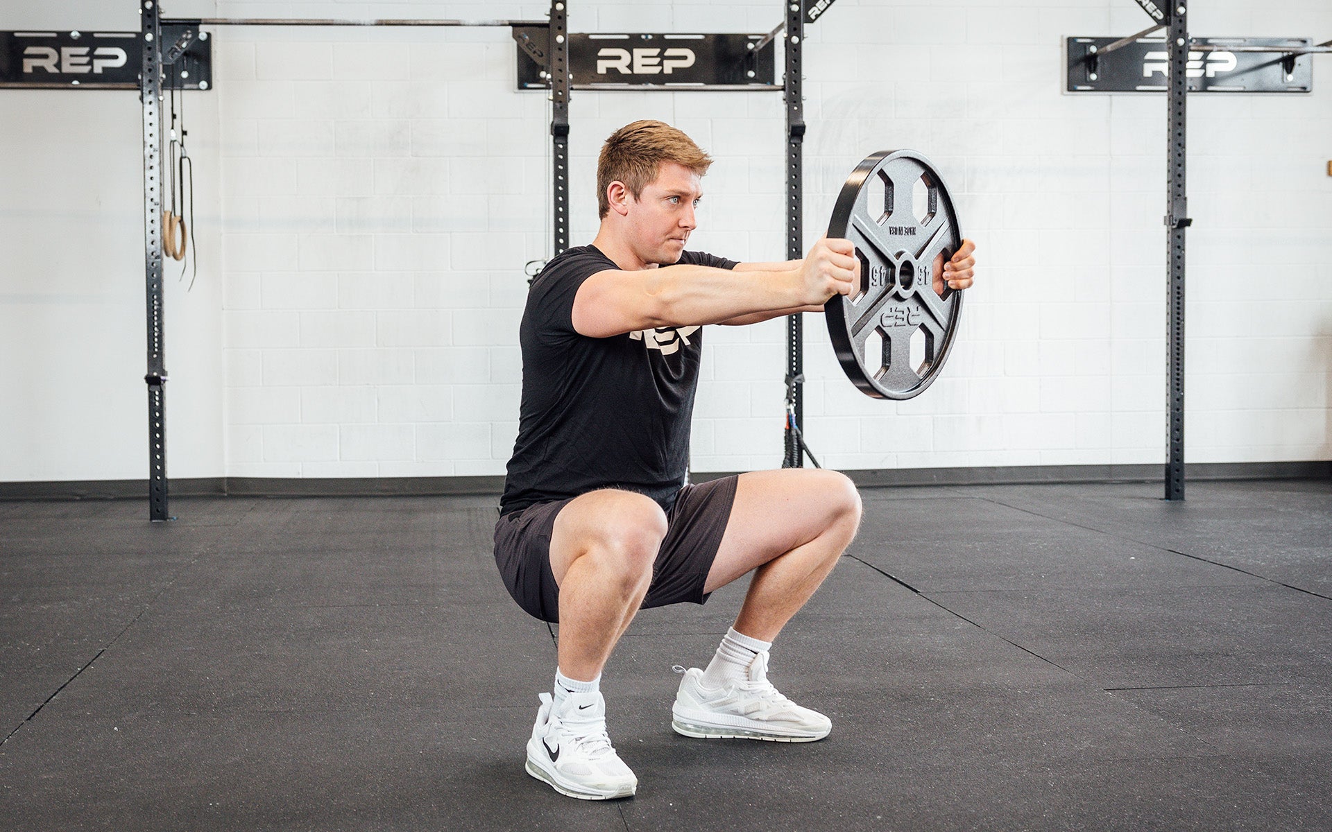 Lifter holding out a single 45lb USA-Made Equalizer Iron Plate in the bottom of a squat.