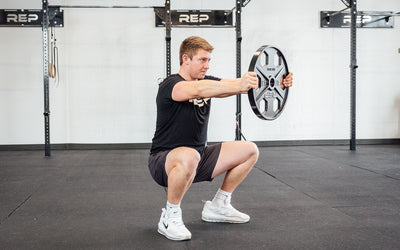 Lifter holding out a single 45lb USA-Made Equalizer Iron Plate in the bottom of a squat.