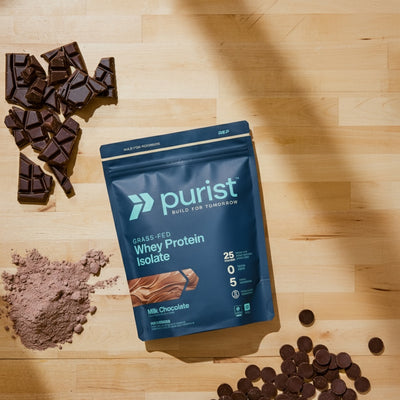 Purist grass-fed whey protein isolate milk chocolate package on a wooden surface with chocolate pieces.