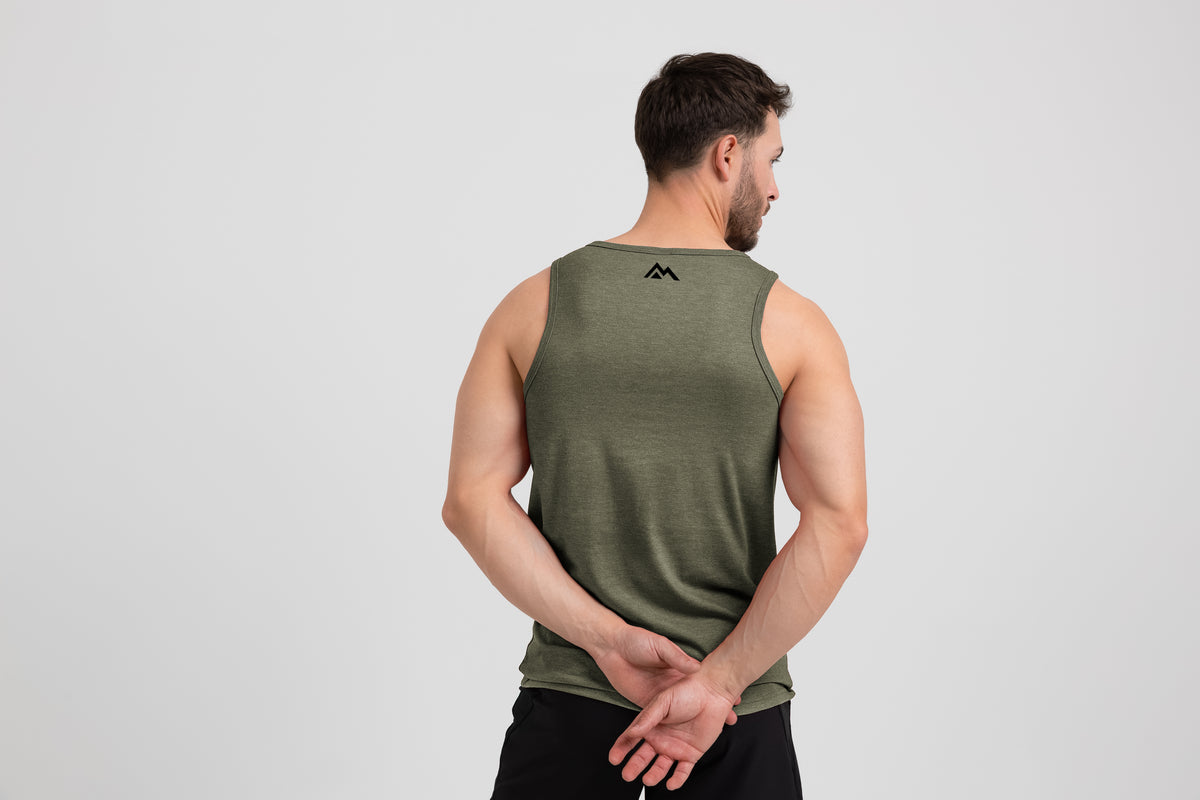 Man wearing the Men's Daily Driver Tri-Blend Tank in Heather Olive with shorts -showing mountain logo on back