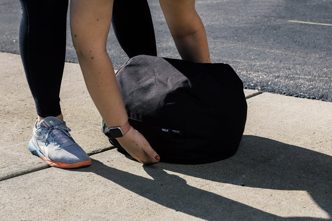 Stone sandbag on ground. Person about to lift it