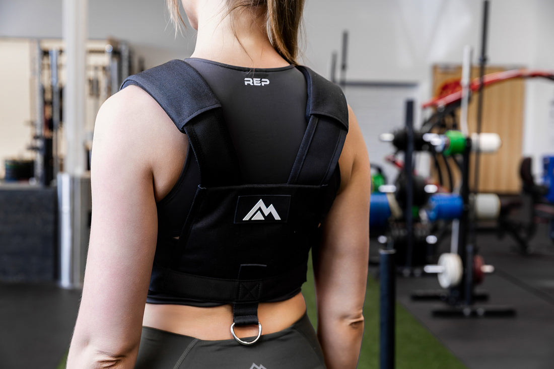Person wearing a black Sled Harness with visible branding (mountain logo on the back) in a gym setting