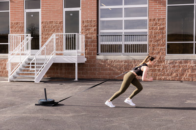 Woman utilizing Sled Harness to pull a sled with weight outside.