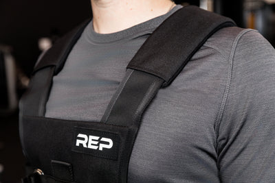 Person wearing black Sled Harness with 'REP' branding in a gym setting