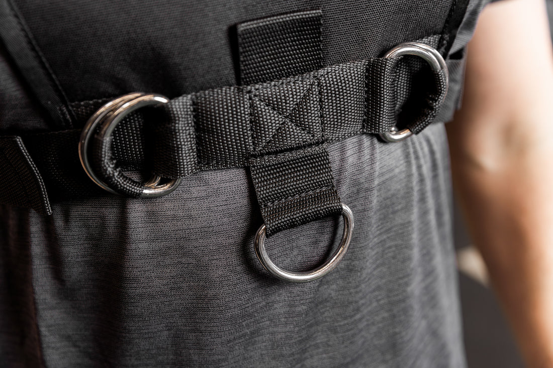 Close-up of a black Sled Harness with D-rings on a person wearing a gray shirt.
