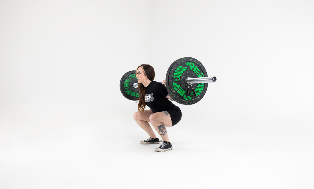 Side view of a lifter in the bottom position of a squat with a barbell in the back rack position loaded with a pair 25lb pinnacle bumper plates.