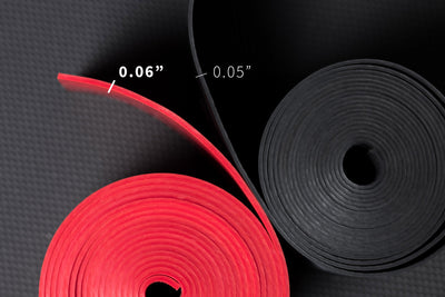 Overhead view a pair of rolled up floss bands showing that the black has a 0.05" thickness and the red has a 0.06" thickness.